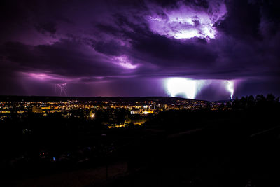 Illuminated cityscape against dramatic sky at night