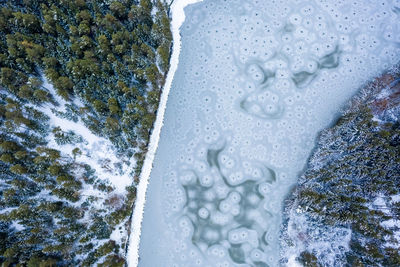 Flight over frozen lake in forest, austria. aerial photography during winter season.