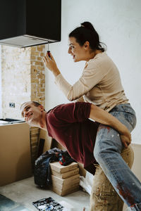 Man piggybacking woman fixing lighting equipment while renovating home together