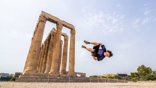 Low angle view of man performing mid-air stunt at old ruined temple against sky