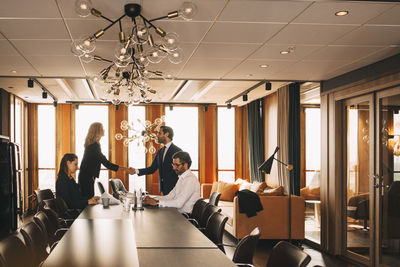 Colleagues shaking hands while lawyers working at table in board room