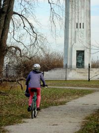 Rear view of woman riding bicycle on pathway against lighthouse