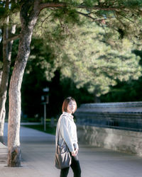 Young woman walking on footpath against trees at park