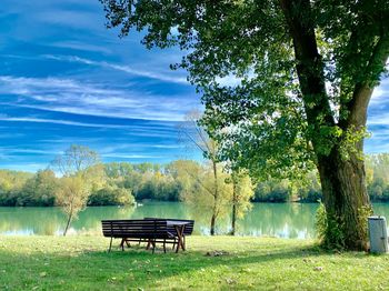 Bench in park by lake against sky