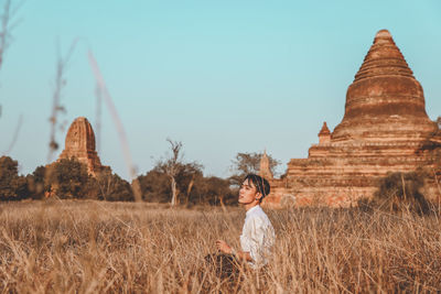 Man sitting on grassy land against temple