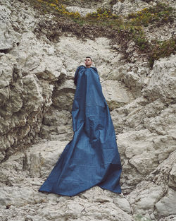 Young man covered with large fabric on rock formation