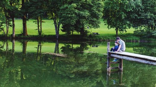 Father with daughter sitting on pier over lake