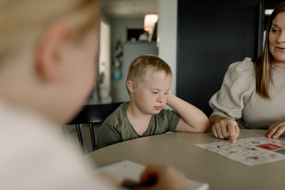 Boy with down syndrome sitting by mother teaching at home