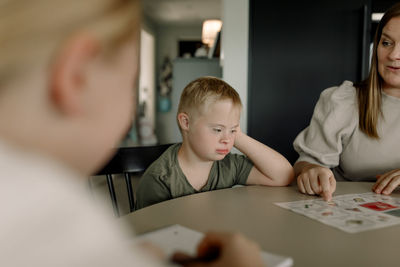 Boy with down syndrome sitting by mother teaching at home