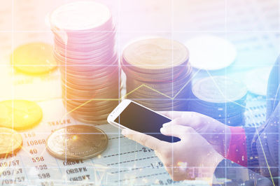 Digital composite image of hands holding using mobile phone with graphs and coins desk