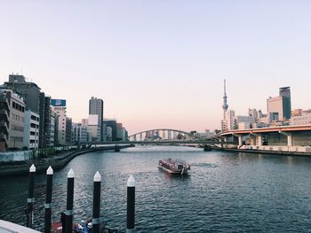 Bridge over river by buildings in city against clear sky