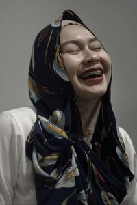 Close-up of happy young woman wearing hijab against gray background