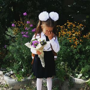 Shy girl holding bouquet while standing against flowering plants