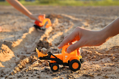 Cropped hands holding earth mover and crane on sand