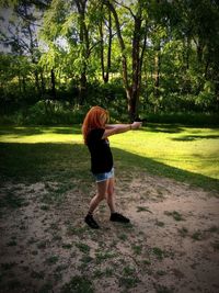 Full length of woman shooting gun in park against trees