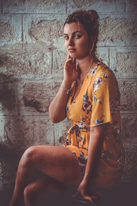 Portrait of young woman sitting on brick wall