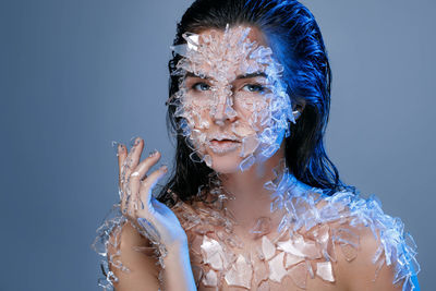 Portrait of woman with broken glass on body against purple background