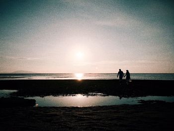 Silhouette people standing on beach against sky during sunset