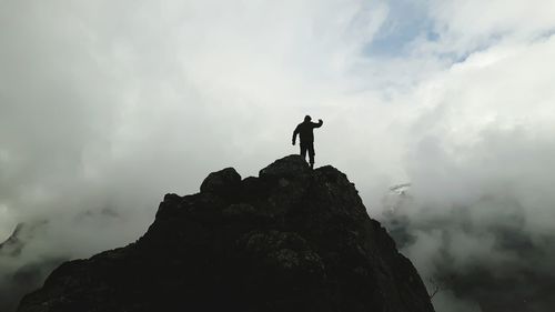 Low angle view of man standing on rock formation against cloudy sky