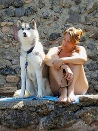 Portrait of young woman with dog sitting on rock