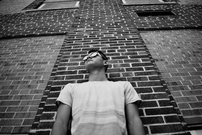 Low angle view of young man standing against brick wall