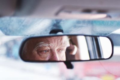 Senior man reflecting on rear-view mirror in car