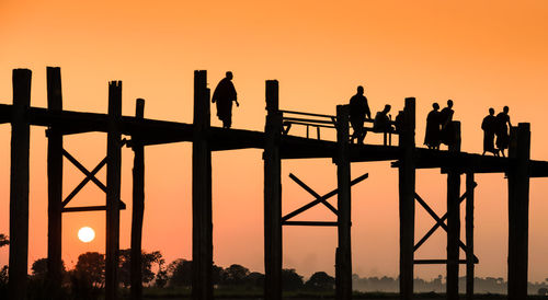 Silhouette people standing on bridge against sky during sunset