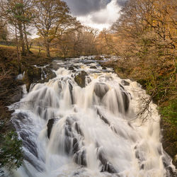 Scenic view of waterfall in forest against sky