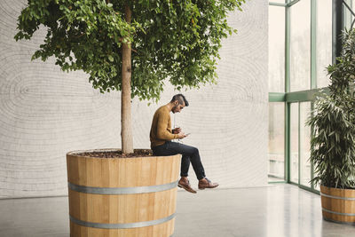 Side view of businessman using mobile phone while sitting on pot in creative office