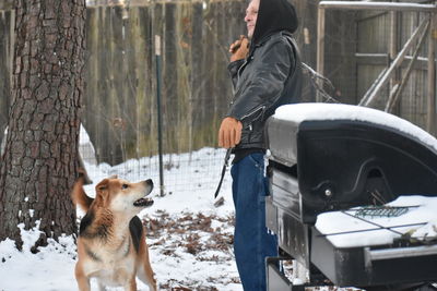 Man with dog standing on snow against wall