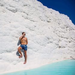 Full length of shirtless man standing on rock formation by lagoon