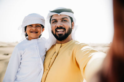 Portrait of father and son doing selfie while standing at desert