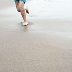 Low section of boy running on wet sand at beach