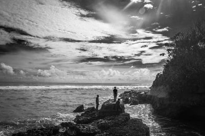 Friends on rock formation in sea against sky