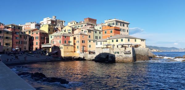 Buildings by sea against clear blue sky