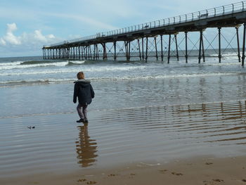 Rear view of boy standing on shore at beach against sky