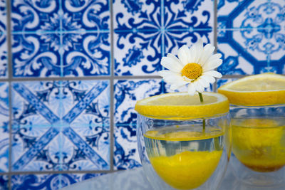 Daisy stuck in fruit slice on glass against blue tiled wall