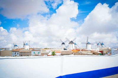 Buildings and windmills against cloudy sky