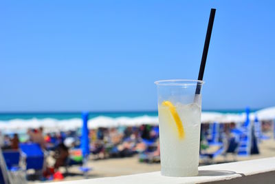 Close-up of drink on table at beach against blue sky