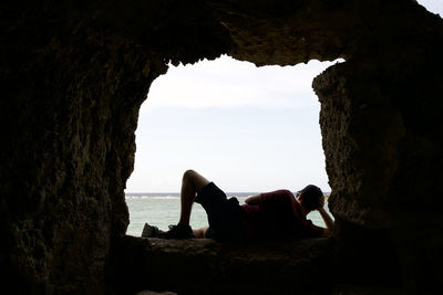 Man sitting on rock by sea against sky