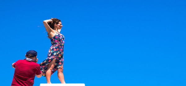 Rear view of photographer standing by fashion model against clear blue sky