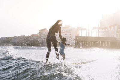 Full view of mother and son surfing a small wave at sea