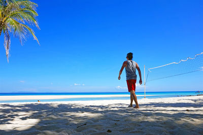 Rear view of man walking by volleyball net at beach against sky