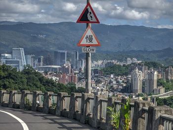 Road sign by buildings in city against sky