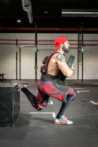 Side view of muscular sportsman in weight vest and with heavy disc doing squats during workout in gym