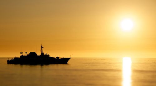 Military frigate sailing on sea at sunset