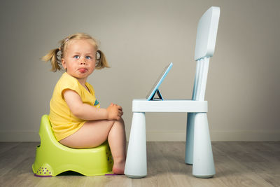 Portrait of young girl sitting on potty with tablet