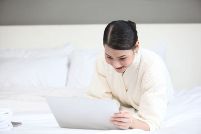 Young woman using mobile phone while sitting on bed at home