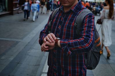 Midsection of man checking time while standing on street in city