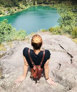 Rear view of woman sitting on rock by lake